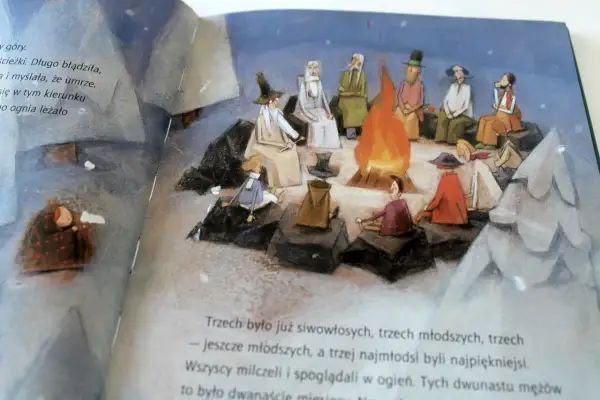 Ilustracja przedstawia grupę ludzi siedzących wokół ogniska, z dzieckiem przykrytym kocem po lewej stronie.